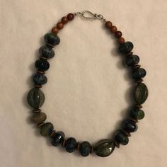 This Betsy Michaels Original Necklace Is Handmade By Betsy Herself. This Necklace Is Made With Stone And Wooden Beads. The Stone Beads Have A Large Range Of Mixed Colors, Which Include Brown, Black, Green, And Blue. The Necklace Is 20.5 Inches From End To End, And It Features A Hook-Style Clasp. Its Color Theme Consists Of Earth Colors. Everyday Wooden Beads Jewelry, Casual Wooden Beaded Necklaces For Jewelry Making, Casual Large Beads For Jewelry Making, Casual Wooden Beads Necklace For Jewelry Making, Unique Everyday Beaded Necklaces, Everyday Bohemian Necklace With Wooden Beads, Everyday Large Beads Necklace, Casual Everyday Jewelry With Wooden Beads, Casual Brown Necklace For Everyday