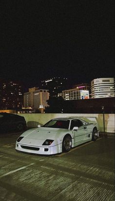 a white sports car parked in an empty parking lot next to some tall buildings at night