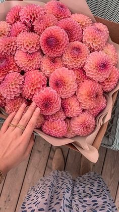 a woman holding a bouquet of pink flowers on top of a wooden floor next to another person's hand