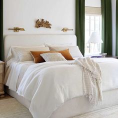 a white bed sitting in a bedroom next to two windows with green drapes on them