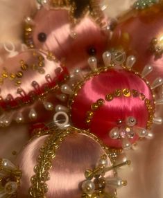 some pink and gold ornaments are laying on a white cloth with pearls, beads and other things