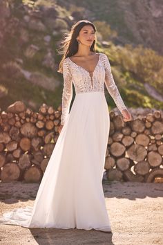 a woman in a white wedding dress standing next to stacked logs and looking off into the distance