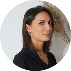 a woman with long dark hair wearing gold earrings and a black top is looking into the camera