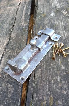 an old metal latch sitting on top of a wooden table next to screws and nails