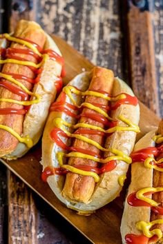 three hot dogs with ketchup and mustard on a wooden tray