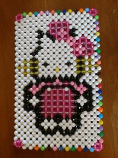 a cross stitch beaded hello kitty design on a wooden table with white and pink beads