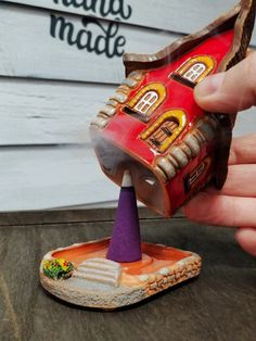 a hand is holding a miniature house in the shape of a shoe with a purple cone sticking out of it