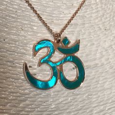 "Om in 18 carat rose gold on 925 silver and acquamarine mother of pearl backdrop. Om is one of the most important spiritual symbols, a sacred sound in Indian religions, found also in some chapters of the Veda. It has variously been associated with concepts of \"cosmic sound\" that celebrates the creative powers of the Universe. Its sound is made up of three syllabes (A-U-M): wakefulness / darkness / present, dream / unconscious / past, deep sleep / future truth. In the jewel The five curves shap Spiritual Rose Gold Jewelry For Meditation, Spiritual Rose Gold Sterling Silver Necklace, Spiritual Rose Gold Sterling Silver Necklaces, Spiritual Style Rose Gold Sterling Silver Necklace, Spiritual Rose Gold Copper Necklace, Rose Gold Jewelry For Festivals Gift, Rose Gold Jewelry For Festivals And Gifts, Festive Rose Gold Jewelry Gift, Spiritual Copper Jewelry For Meditation