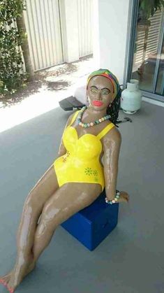 a woman sitting on top of a blue block wearing a yellow bathing suit and beads