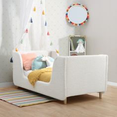 a child's day bed with colorful pillows and blankets on the floor next to a mirror