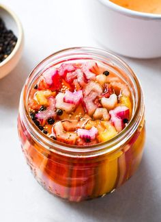 a glass jar filled with food next to two bowls full of beans and carrots