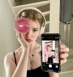 a woman taking a selfie with her cell phone and pink doughnut in front of her face