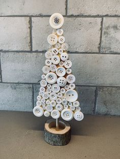 a christmas tree made out of buttons sitting on top of a wooden stand next to a brick wall