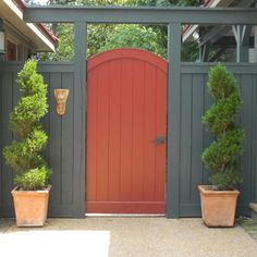 two potted plants are in front of a red door on a gray fenced entrance