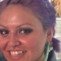 a woman with purple hair is smiling at the camera while wearing ear rings and earrings