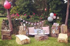 an outdoor party setup with balloons and wooden pallets on the grass in front of trees