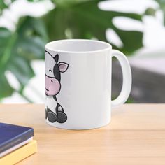 a white coffee mug with a cartoon cow on it sitting on a table next to some books