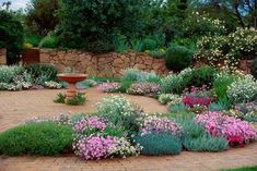 a garden filled with lots of flowers next to a stone wall covered in greenery