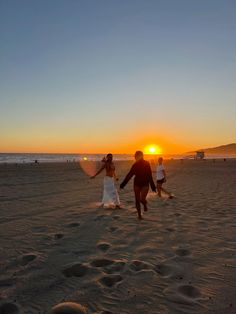 a bride and groom walking on the beach at sunset