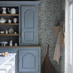 a kitchen with blue cupboards and white counter tops in front of a wallpapered wall