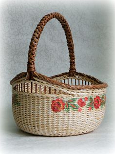 a wicker basket with flowers painted on the side and handles, sitting on a white surface