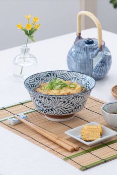 a table topped with bowls and plates filled with food on top of a wooden mat