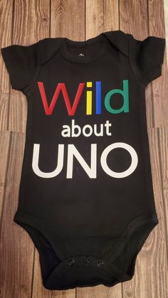 Wild about UNO black Bodysuit IF YOU DO NOT SEE A SIZE YOU NEED PLEASE MESSAGE ME AND I WILL TRY TO ACCOMMODATE YOUR ORDER. 12 month LONGSLEEVE also available  leave a message for this request in the note box WHAT YOU WILL RECEIVE:  ♥ as described in the example photo above.  HOW TO ORDER:  ♥ Choose your size  ♥ Add to cart. ♥ Please include any special instructions in the notes to seller box at checkout.  CARE INSTRUCTIONS: All of my products are made with a high quality heat transfer vinyl then pressed with a professional heat press, ensuring the vinyl will not flake or peel when washed. ♥ Turn inside out ♥ Machine wash cold on delicate cycle/handwash ♥ Tumble dry on low heat ♥ Do not bleach/dry-clean ♥ Do not iron directly onto the design. IMPORTANT INFORMATION: ♥ If you do not see a si Black Letter Print T-shirt For Playtime, Black T-shirt With Letter Print For Playtime, Black Top With Text Print For Birthday, Black Tops With Text Print For Birthday, Black Family Matching T-shirt For Playtime, Funny Black Tops For Gender Reveal, Fun Black Party T-shirt, Fun Black T-shirt For Party, Black Fun T-shirt For Casual Party