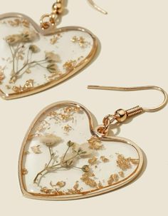 two heart shaped earrings with dried flowers in them on a white surface, one is gold and the other is clear