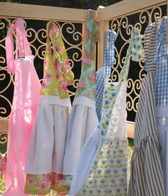 several aprons hanging on a rack in front of a fence