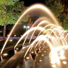 a water fountain is lit up in the night with bright lights on it's sides