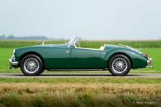 a green sports car driving down a road next to a lush green grass covered field