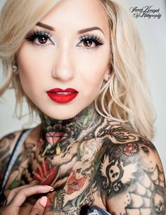 a woman with tattoos on her chest holding a cell phone and looking at the camera