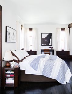 a bedroom with white walls and wood flooring is pictured in this image, there are two windows on the far side of the bed