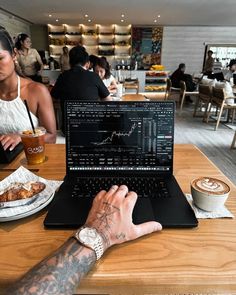 a man sitting in front of a laptop computer on top of a wooden table next to a cup of coffee