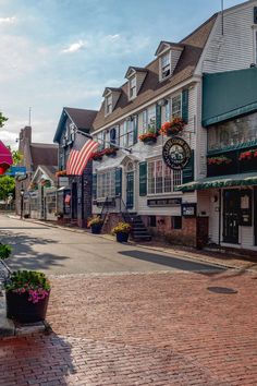 an empty street lined with shops and flowers in front of buildings on either side of the road