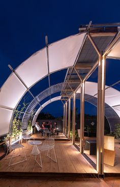 an outdoor covered patio area with chairs and tables at night, lit up by lights