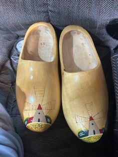 two wooden shoes with painted designs on them are sitting on a gray couch next to a person's feet