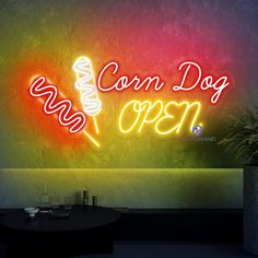 a neon sign that says corn dog open on the wall next to a potted plant