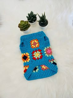 a blue crocheted bag with flowers on it sitting on a white rug next to potted plants