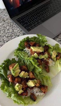 two lettuce wraps with chicken and avocado on top, next to a laptop