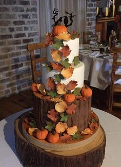 a three tiered cake decorated with fall leaves and pumpkins on a wooden stand