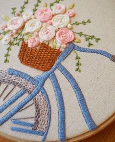 a close up of a embroidery on a wooden surface with a bicycle and flowers in the basket