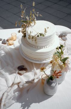 a white wedding cake sitting on top of a table next to vases filled with flowers