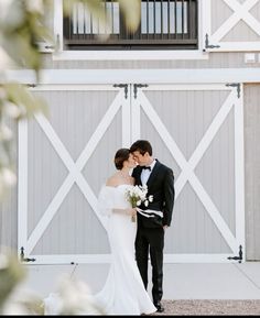 a bride and groom standing in front of a barn door with their arms around each other