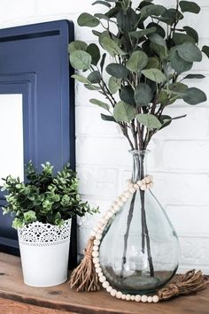 a vase filled with green plants on top of a wooden table next to a potted plant