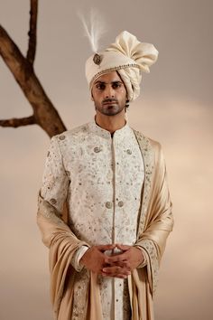 a man wearing a white turban standing in front of a tree with his hands on his hips