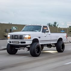 a white truck driving down the road with big tires on it's front wheels