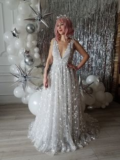 a woman in a white dress standing next to some balloons and silver foil star decorations