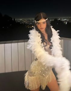 a woman in a white feathered jacket and headband posing for the camera at night