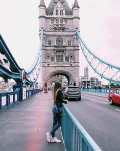 a woman standing on the side of a bridge with cars passing by in front of her